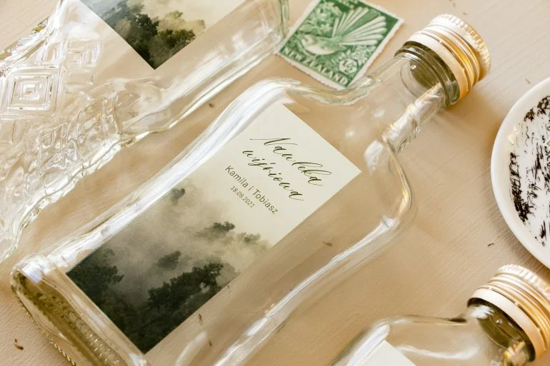 Szklane butelki z grafiką leśną na etykiecie | Upominki ślubne dla gości