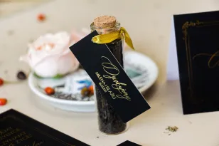 Geschenke für Gäste in Form von Teeflaschen. Schwarzes Glamour-Etikett mit goldenem Text und goldenem Rahmen