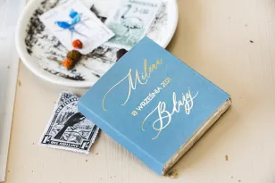 Geschenke für Hochzeitsgäste in Form von Milchschokolade, Deckblatt in staubigem Blau mit kalligraphischer, goldener Schrift