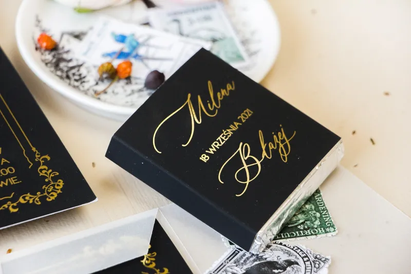 Prezenty dla gości weselnych w postaci mlecznej czekoladki, czarna owijka w stylu glamour ze złotym tekstem oraz złotą ramką