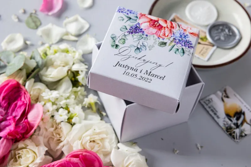 Eine Schachtel für Süßigkeiten für Hochzeitsgäste in Form eines Würfels mit Grafiken aus Pfingstrosen und Flieder