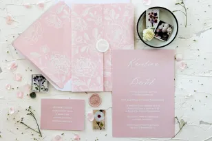Zarte Hochzeitseinladungen in puderrosa Farbe, weißer Pfingstrosendruck auf der Verpackung