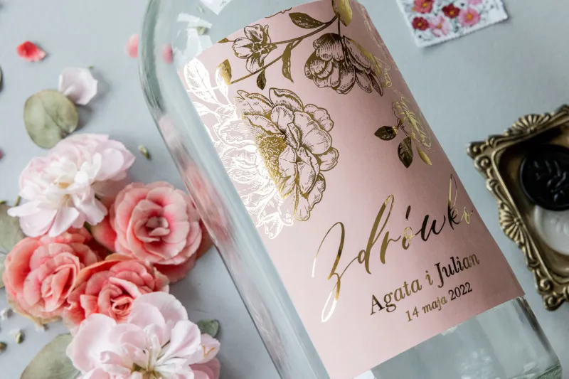 Etykiety samoprzylepne na butelki weselne na alkohol w kolorze pudrowego różu ze złotą grafiką piwonii