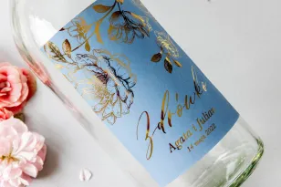 Etykiety samoprzylepne na butelki weselne na alkohol w kolorze dusty blue ze złotą grafiką kwiatów.
