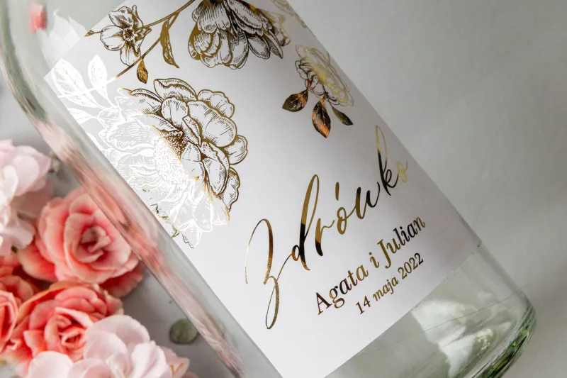Etykiety samoprzylepne na butelki weselne na alkohol w białym kolorze ze złotą grafiką piwonii.