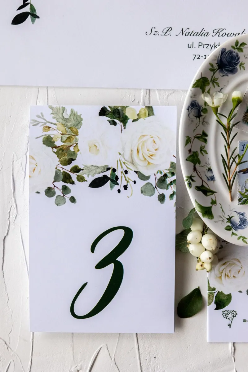 Numery stolików weselnych z kwiatowym motywem białych róż i zielonymi gałązkami eukaliptusa