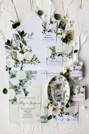 Elegante Hochzeitseinladungen auf Glas mit einem floralen Motiv aus weißen Rosen und grünen Eukalyptuszweigen.