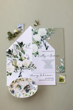 Eleganckie zaproszenia ślubne na szkle z kwiatowym motywem białych róż i zielonymi gałązkami eukaliptusa.