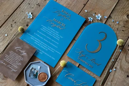 Moderne Hochzeitseinladungen auf staubblauem Glas mit vergoldeten Vor- und Nachnamen des Brautpaares