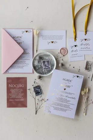 Weiße, klassische Hochzeitseinladungen mit goldenem Inhalt. Die Einladungen werden von einem puderrosa Umschlag begleitet