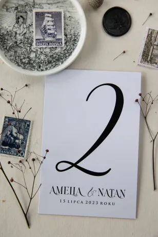 Klassische Tischnummern mit schwarzer dekorativer Schrift auf weißem Hintergrund von Amelia-Wedding.pl