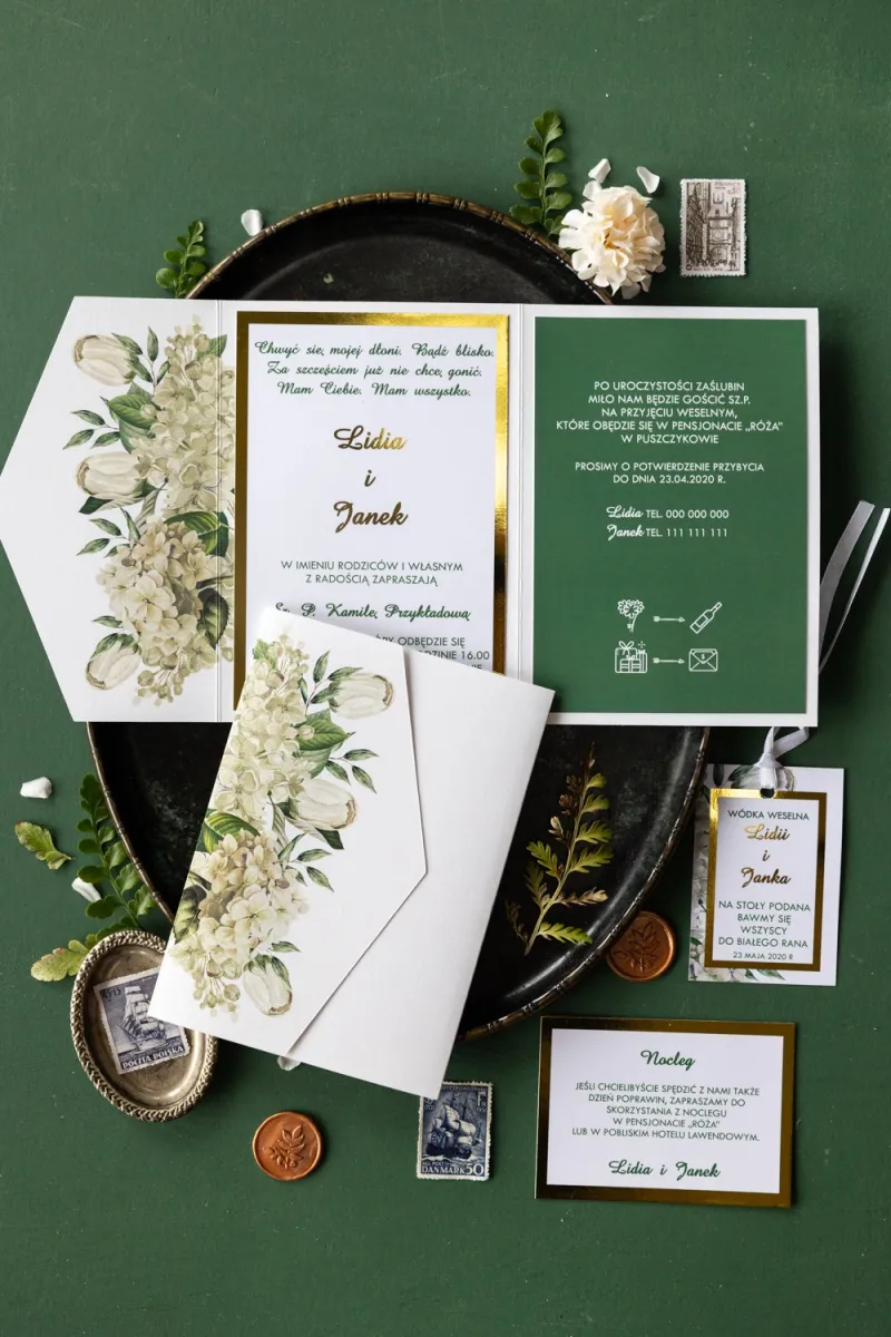 Złote zaproszenia ślubne z białą hortensją i tulipanami w otoczeniu zieleni