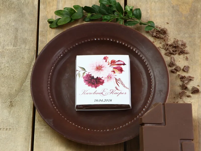 Podziękowanie dla gości weselnych w postaci mlecznej czekoladki, owijka z grafiką kwiatów dalii w barwach bordo i jasnego różu.