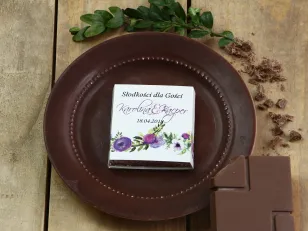 Podziękowanie dla gości weselnych w postaci mlecznej czekoladki, owijka z grafiką fioletowych kwiatów w różnych odcieniach.