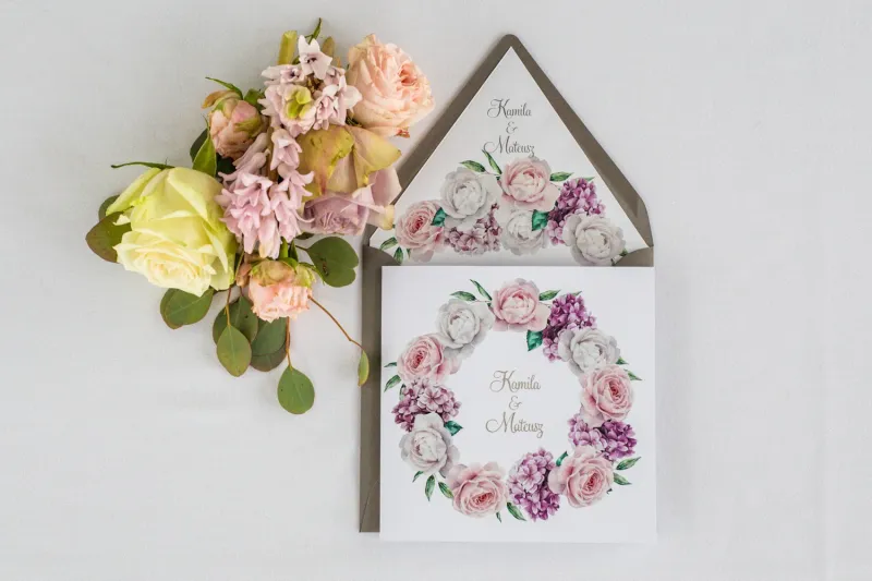 Zaproszenia ślubne z srebrnymi napisami. Wianek z białymi i różowymi piwonia oraz kwiatami bzu