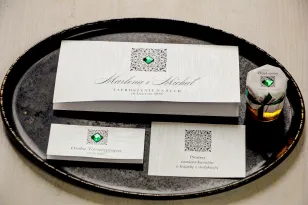 Silberne Hochzeitseinladungen mit einem dekorativen, smaragdgrünen Kieselstein. Das Ganze ist auf einseitigem Perlenpapier gefer