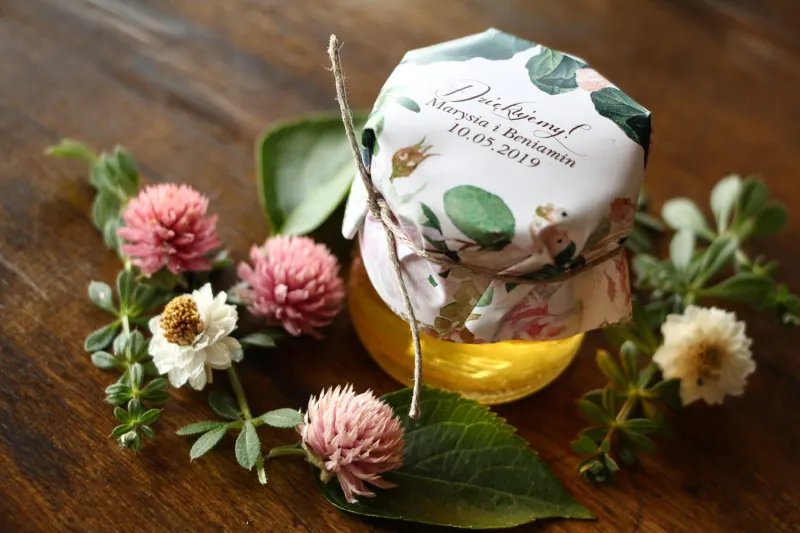Süßes Dankeschön an die Hochzeitsgäste in Form von Gläsern mit Honig mit einem Motiv aus pastellrosa Dahlien und Rosen