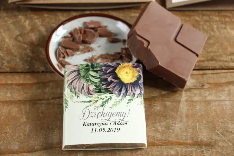 Podziękowanie dla gości weselnych w postaci mlecznej czekoladki, owijka z astrami w odcieniach fioletu oraz gałązkami paproci