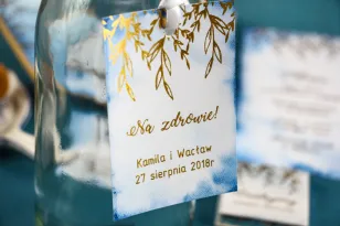 Niebieskie zawieszki na butelki weselne ze złoceniami.