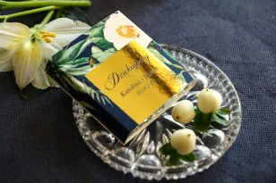 Danke an die Hochzeitsgäste in Form von Schokolade. Goldenes, marineblaues Deckblatt mit weißer Kamelie und grünen Blättern