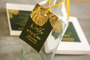 Vergoldete Kleiderbügel für Hochzeitsflaschen im Glamour-Stil. Eine elegante Kombination aus Grün und vergoldeten Monstera-Blätt