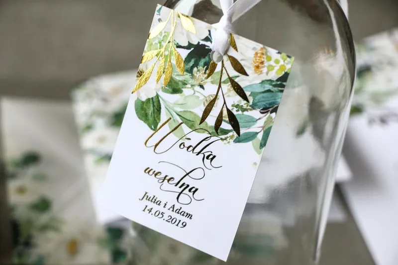 Biało-zielone zawieszki na butelki weselne ze złoconymi gałązkami w stylu glamour, motyw delikatnych, białych kwiatów i zieleni