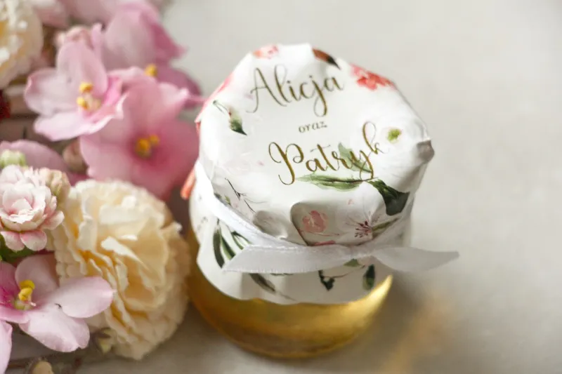 Słoiczek z miodem - podziękowanie dla gości weselnych. Kapturek ze złoconymi napisami oraz z pudrowymi, różowymi kwiatami róży