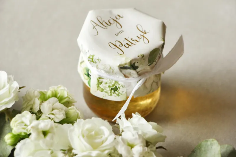 Słoiczek z miodem - słodkie podziękowanie dla gości weselnych. Kapturek ze złoconymi napisami oraz z białymi różami