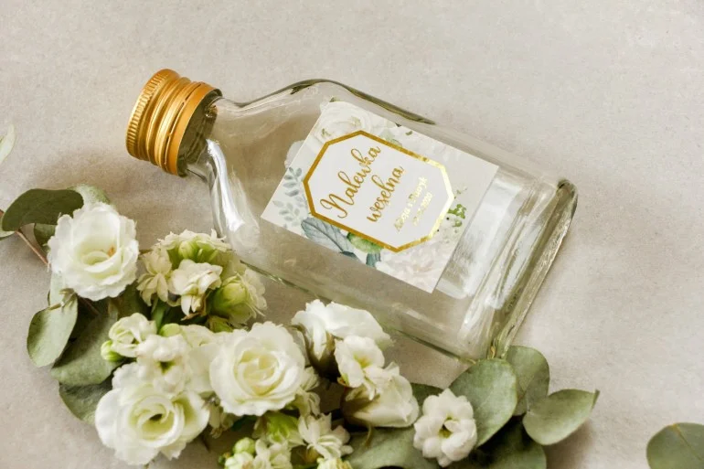 Butelki Weselne z Etykietą w Stylu Glamour i Złoceniami | Prezenty dla Gości z Białymi Kwiatami