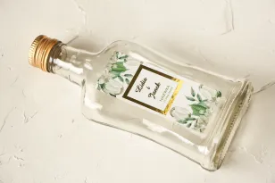 Butelki na nalewki wraz ze złoconą etykietą oraz z białą hortensją i tulipanami w otoczeniu zieleni