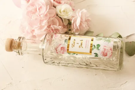 Butelki na nalewki wraz ze złoconą etykietą oraz z różowymi piwoniami w towarzystwie białych róż i zieleni