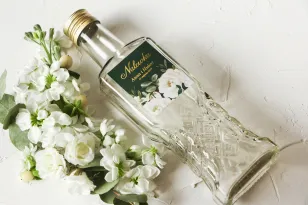 Hochzeitstinkturflaschen mit vergoldetem Etikett und einem eleganten Bouquet aus weißen Rosen und Pfingstrosen mit Eukalyptuszus