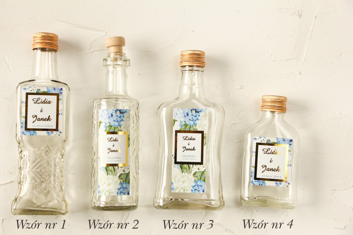 Bottigliette per liquori con etichetta dorata e ortensia blu e bianca circondata da verde