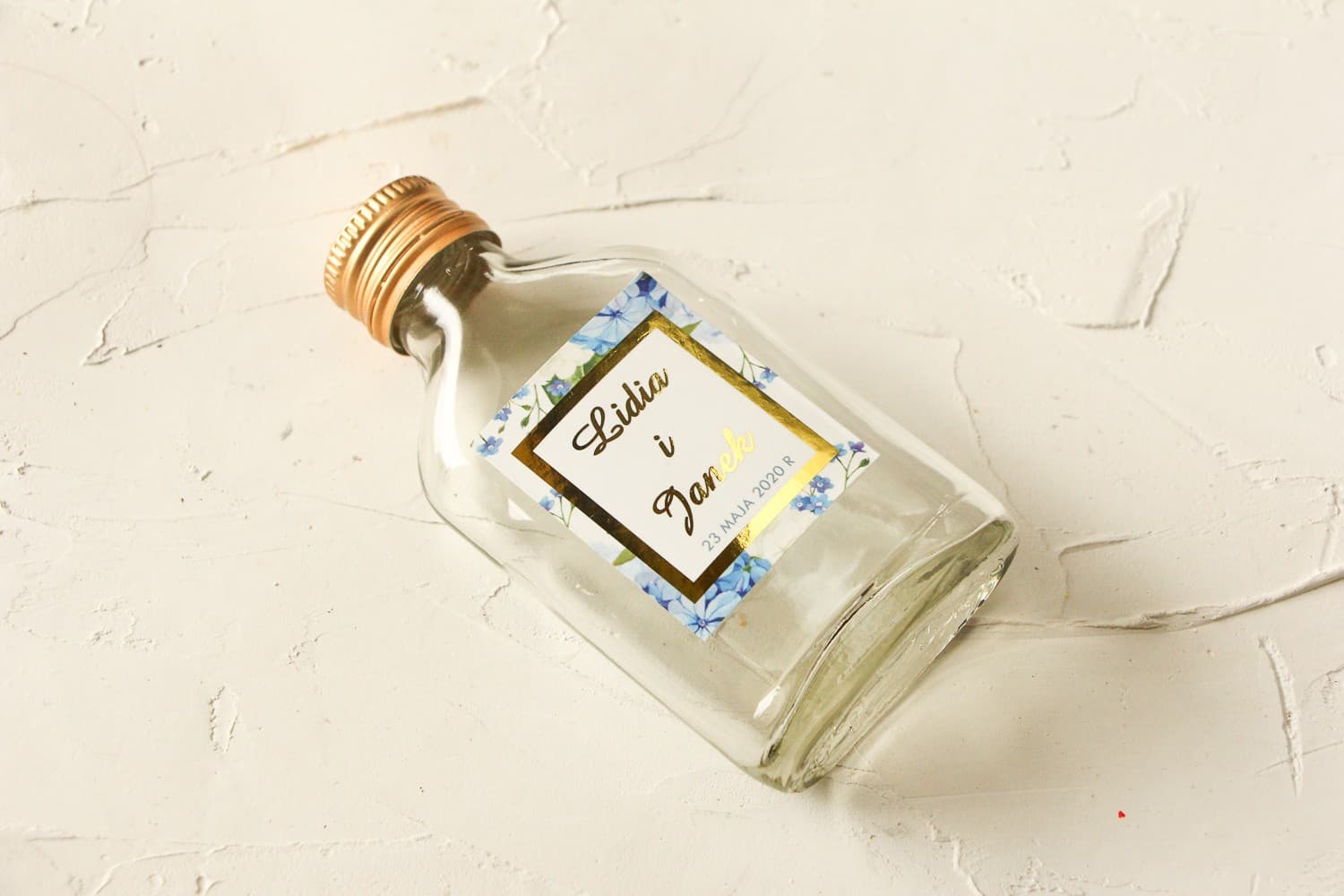 Bottigliette per liquori con etichetta dorata e ortensia blu e bianca circondata da verde