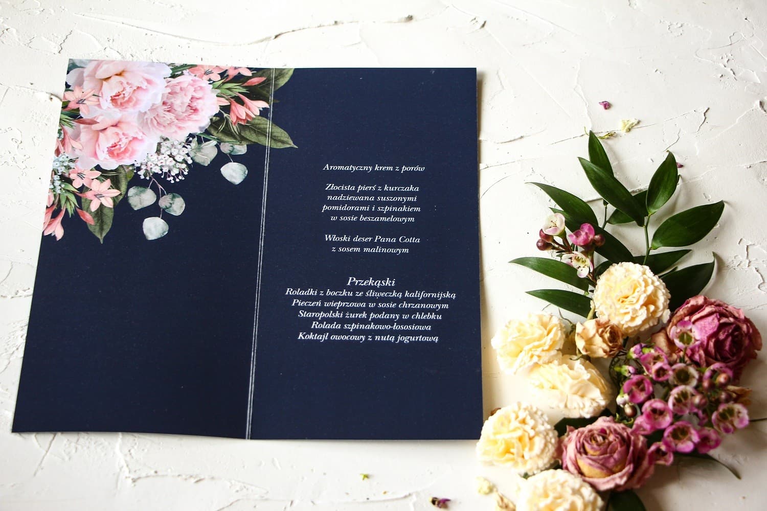 Detalle de menú de boda azul marino con diseño de peonías y letras plateadas