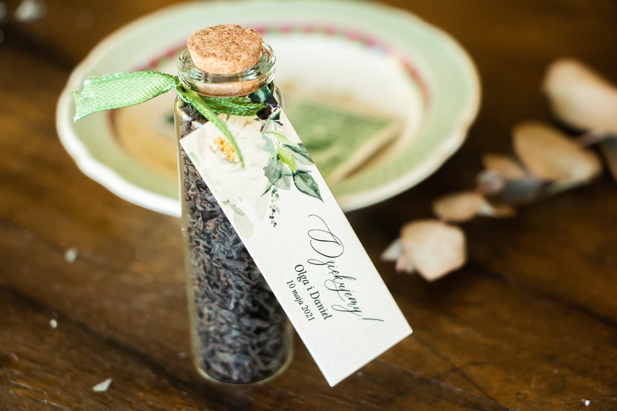Detalles para invitados en forma de botellitas con té, etiqueta con flores blancas y ramitas decorativas
