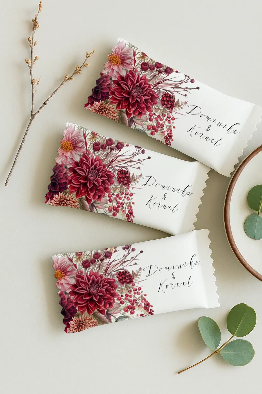 Caramelle mou personalizzate con dalia borgogna weselna Primo piano su involucro caramella mou nuziale con nomi degli sposi e motivo acquarellato di fiori rossi e frutti di bosco.