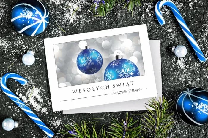 Christmas card with blue baubles decorated with white snowflakes against a background of blurred festive lights.