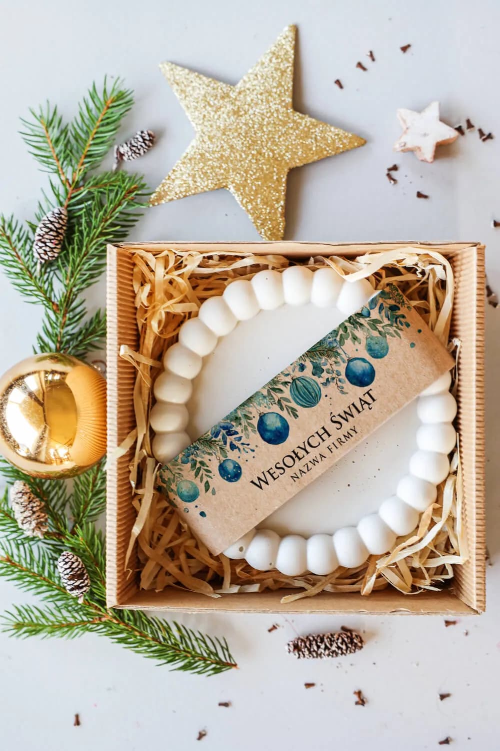 Composición navideña con box de regalo corporativo, estrella dorada y piñas sobre fondo claro.