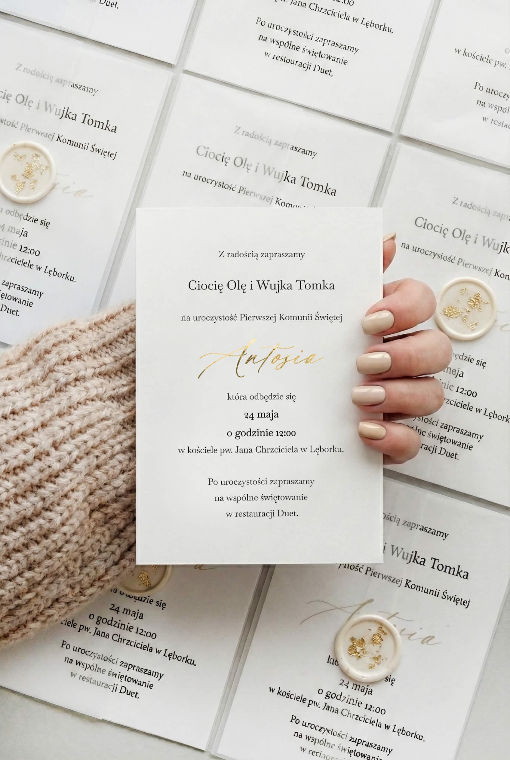 Mano sosteniendo una invitación de comunión Ofelia n.º 5 con lacre crema y copos de oro sobre papel vegetal.