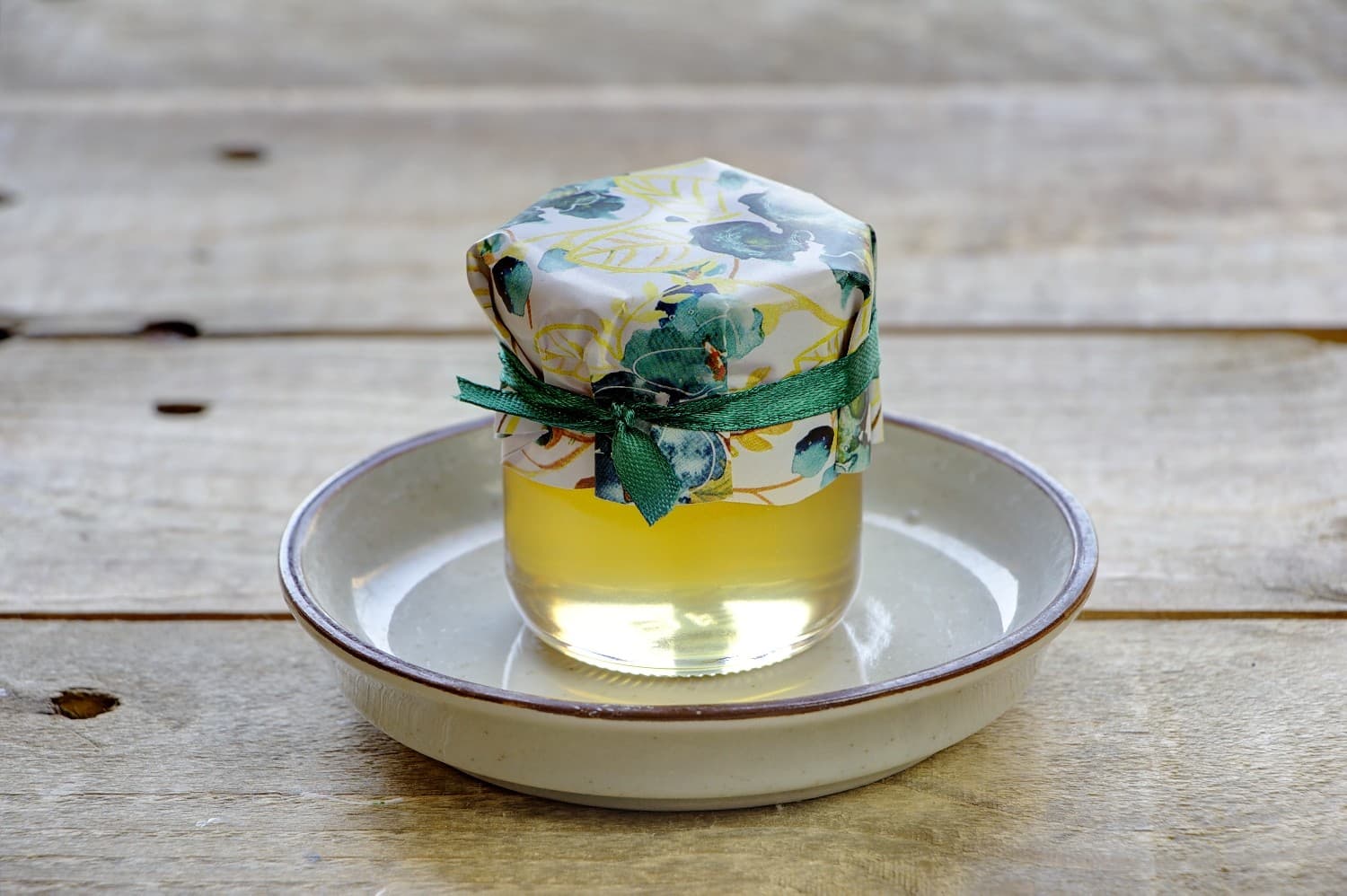 Süße Gastgeschenke für die Hochzeit in Form von Honiggläsern mit smaragdgrüner Blumenkomposition.