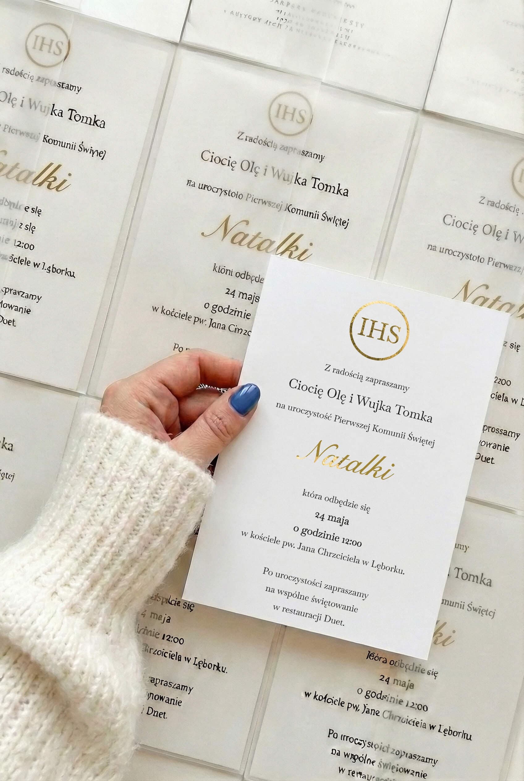 Invitación de comunión dorada con el símbolo IHS y el nombre del niño sostenida en la mano