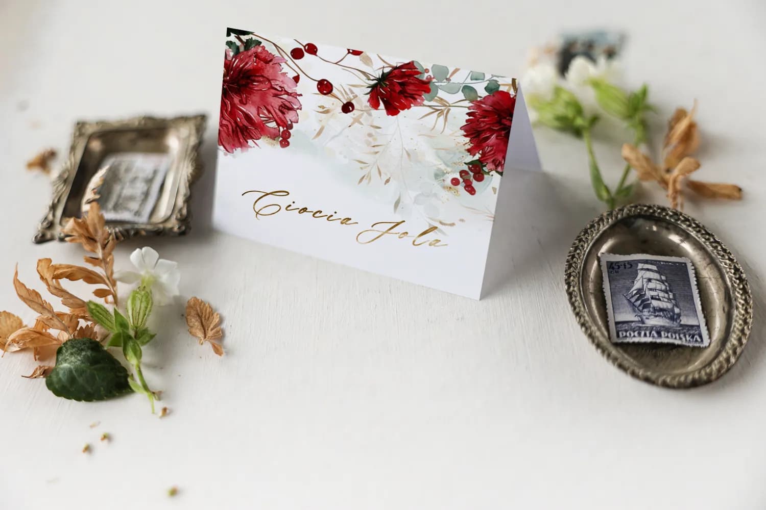 Marcasitios dorado para mesa de boda con nombre del invitado y motivo artístico de flores rojas en acuarela.