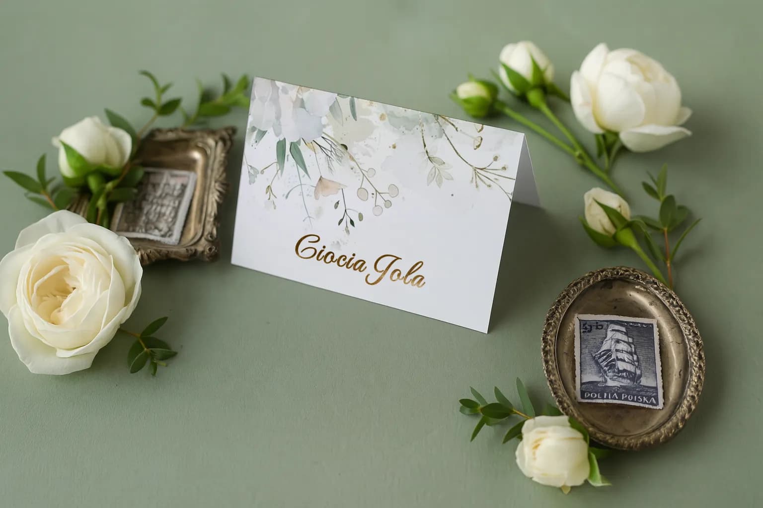 Marque-place doré Ruskus n° 6 Marque-place de mariage élégant Ruskus n° 6 avec inscription dorée sur fond vert sauge entouré de roses blanches.