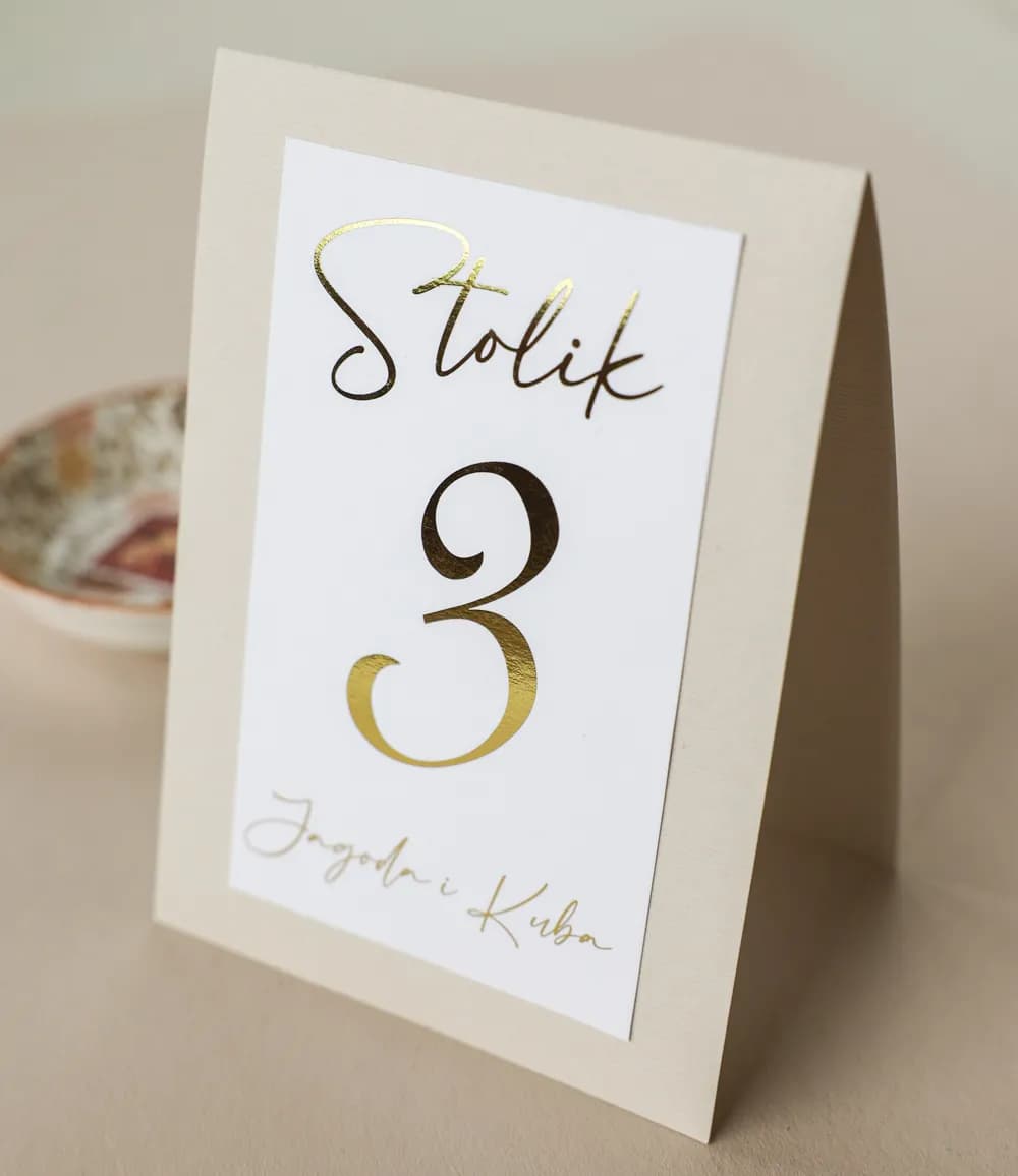 Elegante número de mesa de boda en delicado color beige con etiqueta personalizada y detalles dorados.