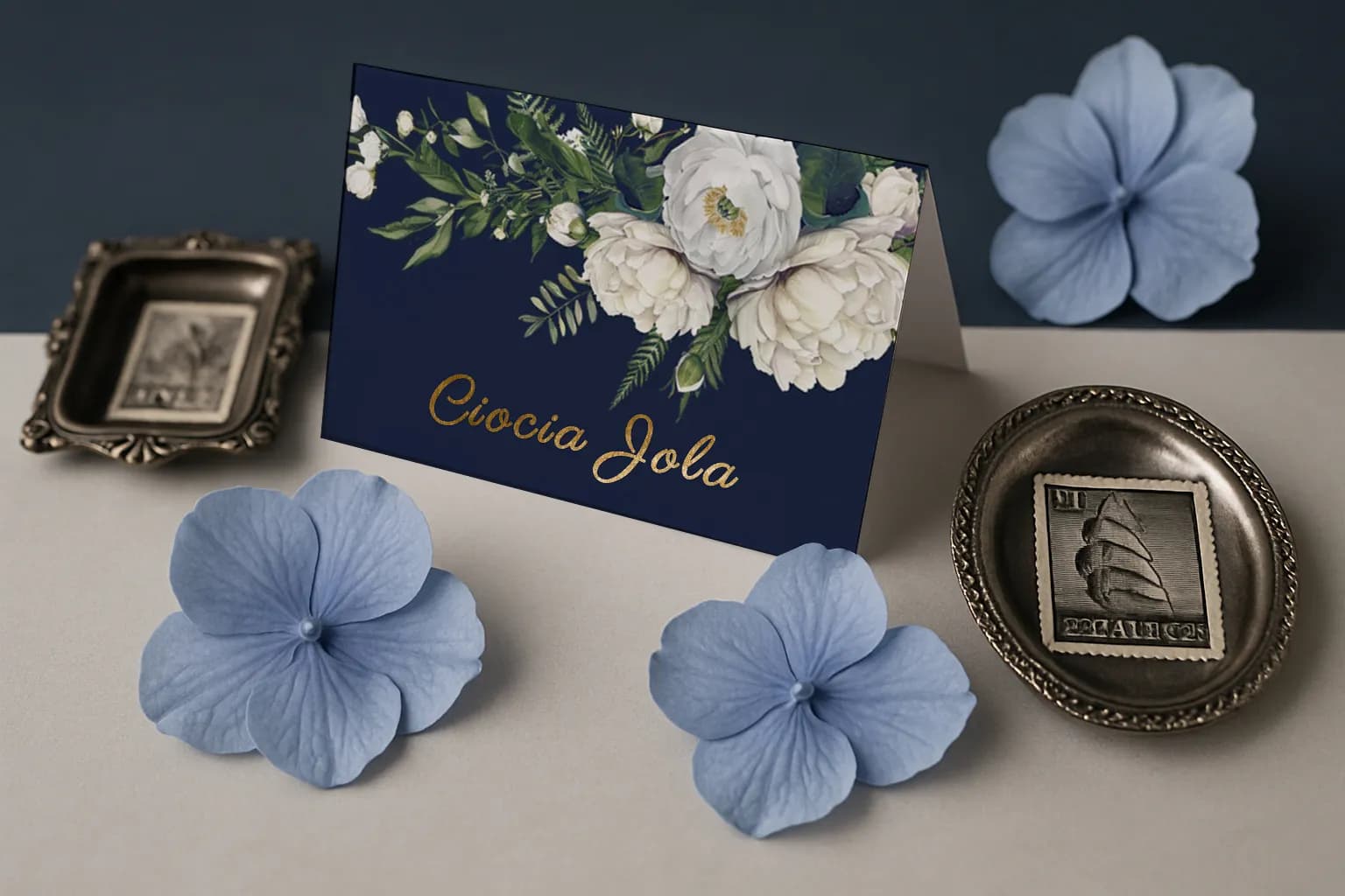 Dettaglio su nome personalizzato dorato su segnaposto navy da tavolo, con dettaglio di fiori bianchi acquerello. Dettaglio su nome personalizzato dorato su segnaposto navy da tavolo, con dettaglio di fiori bianchi acquerello.