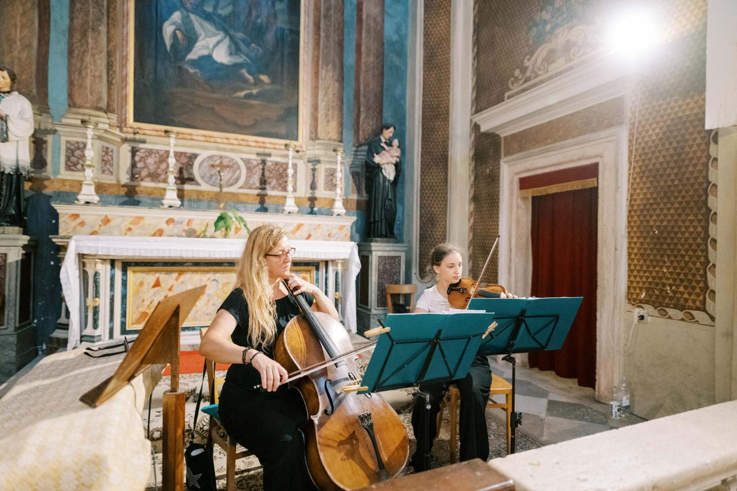 Zdjęcie kobiet grających na wiolonczeli i skrzypcach, siedzących na krzesłach w kościele